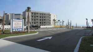 Un estacionamiento con un letrero que indica Estacionamiento Playa en el Parque Argosy, un edificio de varios pisos y palmeras a lo largo de la carretera.
