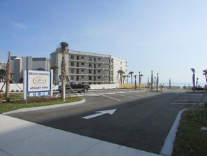 A parking lot with a sign for Beach Parking at Argosy Park, a multi-story building, and palm trees along the roadside. - Cozy Beach Home, WIFI, Turnkey, Walk to the Beach (Ormond Beach)