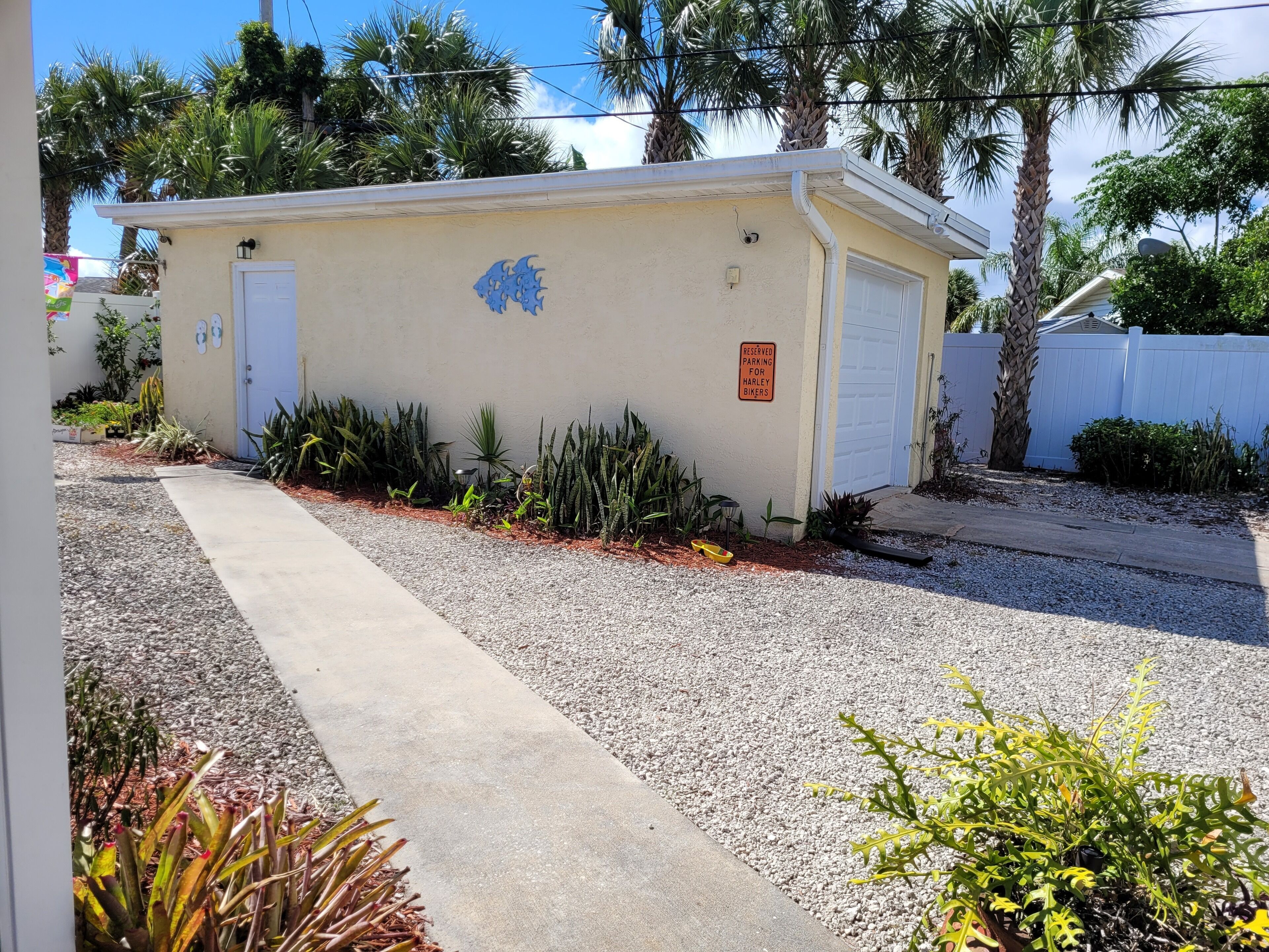 A small building with a garage door, surrounded by gravel and plants.