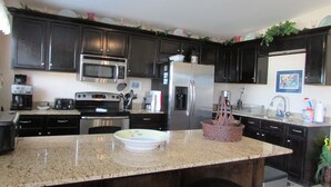 Una cocina con armarios de madera oscura, electrodomésticos de acero inoxidable, encimera de granito y una isla central con taburetes.