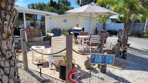 Una casa de playa con mobiliario exterior, un letrero que dice 'BEACH HOUSE' y una estatua de flamenco.