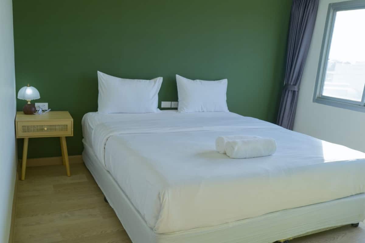 A neatly made bed with white linens in a room with green walls and a wooden floor.