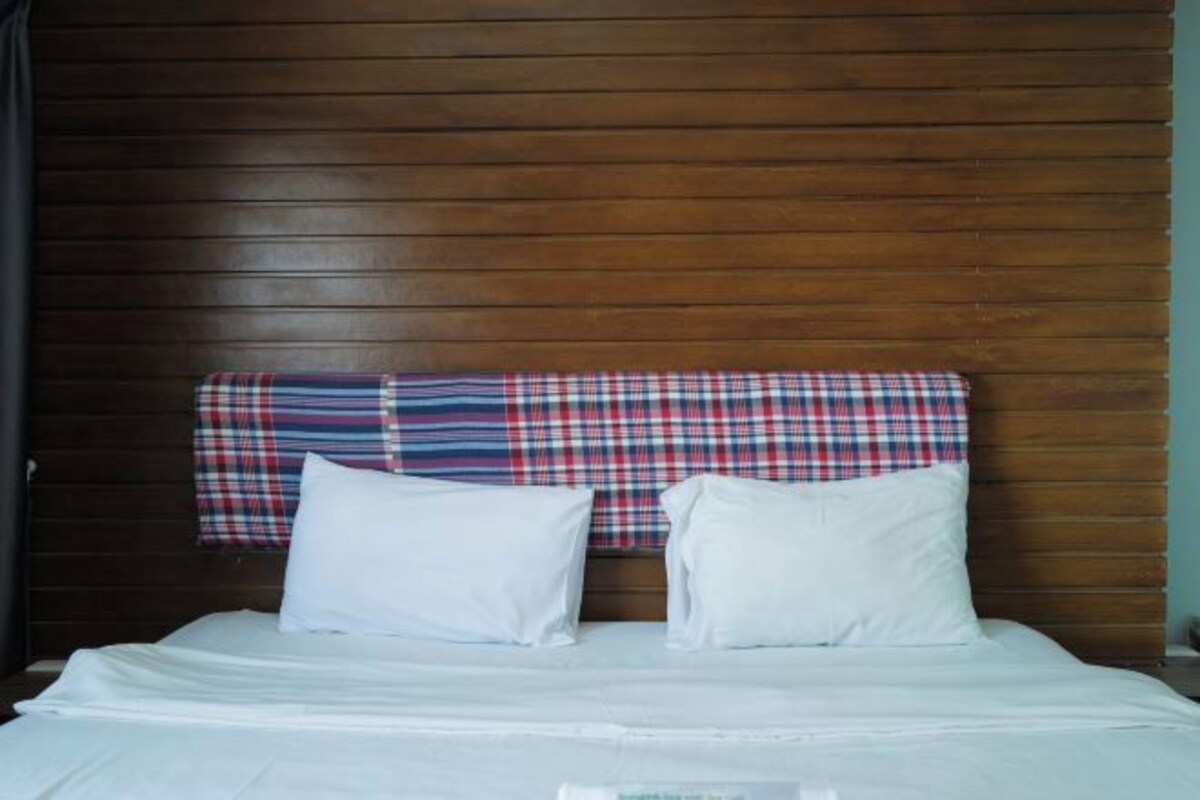 Una cama con ropa de cama blanca y dos almohadas, un cabecero de madera y un tapiz con estampado escocés.