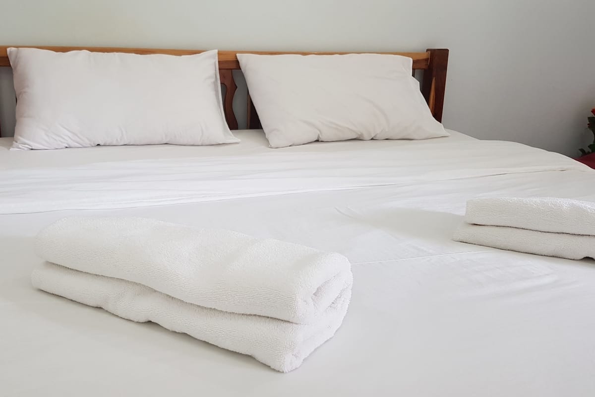 A neatly made bed with white linens and pillows, and two rolled towels on the bed.