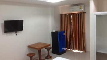 Een hotelkamer met een bed, een houten tafel met twee krukken, een aan de muur bevestigde televisie, een blauwe koelkast en een raam met bruine gordijnen.