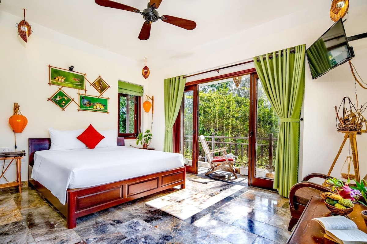 Une chambre spacieuse avec un grand lit, un ventilateur de plafond et une vue sur l’extérieur grâce à une porte-fenêtre coulissante.