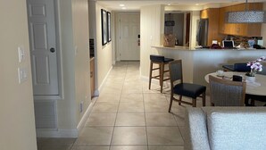 Une cuisine moderne dotée d’un îlot central, d’un coin repas avec deux chaises et d’un couloir menant à une porte.