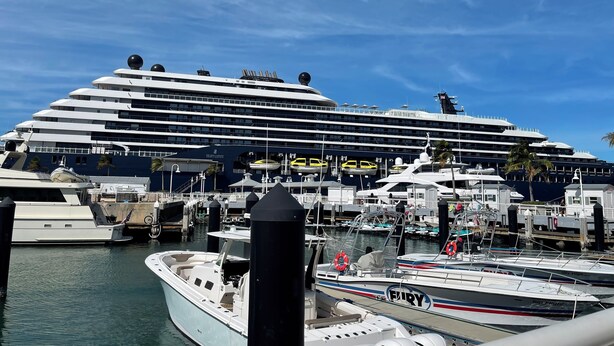 Un grand navire de croisière était amarré dans une marina, où se trouvaient également des bateaux plus petits, sous un ciel bleu et dégagé.