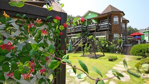 A wooden house with a balcony, a swing set, and a garden with a wooden fence. - Princess Pension (Gyeongju)
