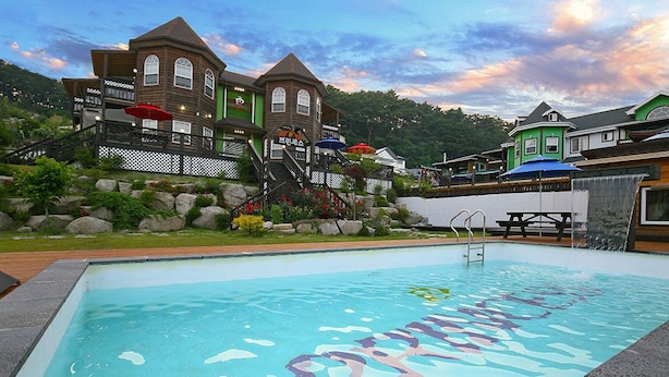 A swimming pool with a wooden deck, a staircase leading to a building with multiple windows, and a view of the surrounding area. - Princess Pension (Gyeongju)