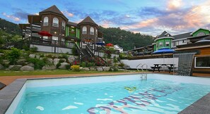 A swimming pool with a wooden deck, a staircase leading to a building with multiple windows, and a view of the surrounding area. - Princess Pension (Gyeongju)