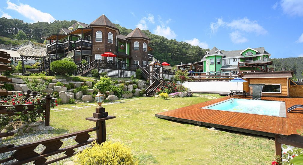 A resort with multiple buildings, a wooden deck, a swimming pool, and a rocky garden area.