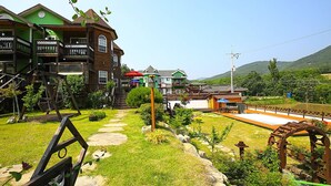 A traditional wooden house with multiple balconies, a stone pathway, and a small garden with a wooden archway. - Princess Pension (Gyeongju)