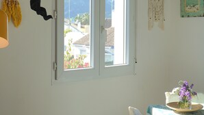 A room with a large window, a hanging macrame piece, a macrame wall hanging, and a vase with flowers on a table. - Beautiful apartment near the beach with a view of the pool and the mountain 'Segaria' (El Verger)