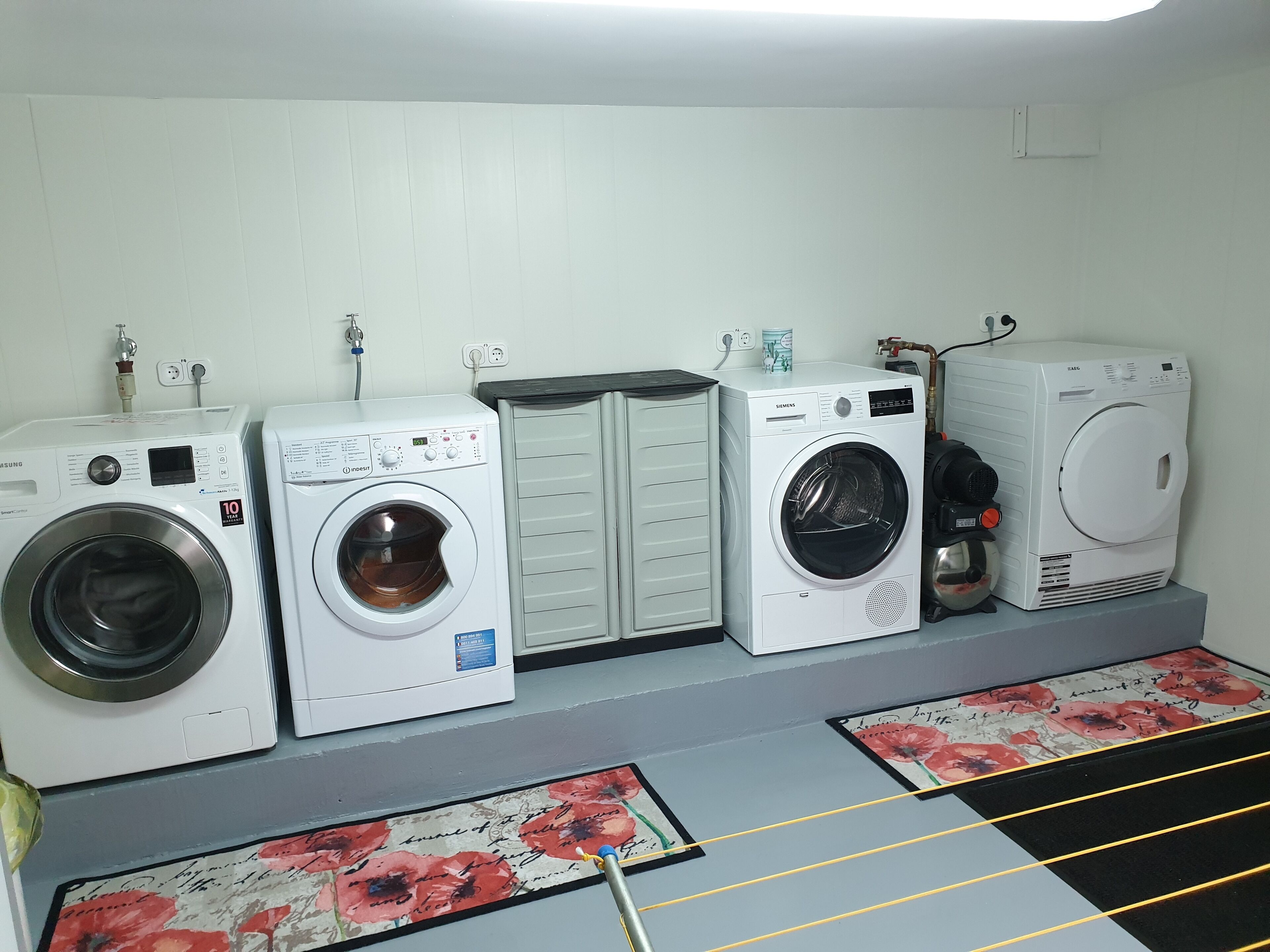 A laundry room with four washing machines, a drying machine, and a cabinet.