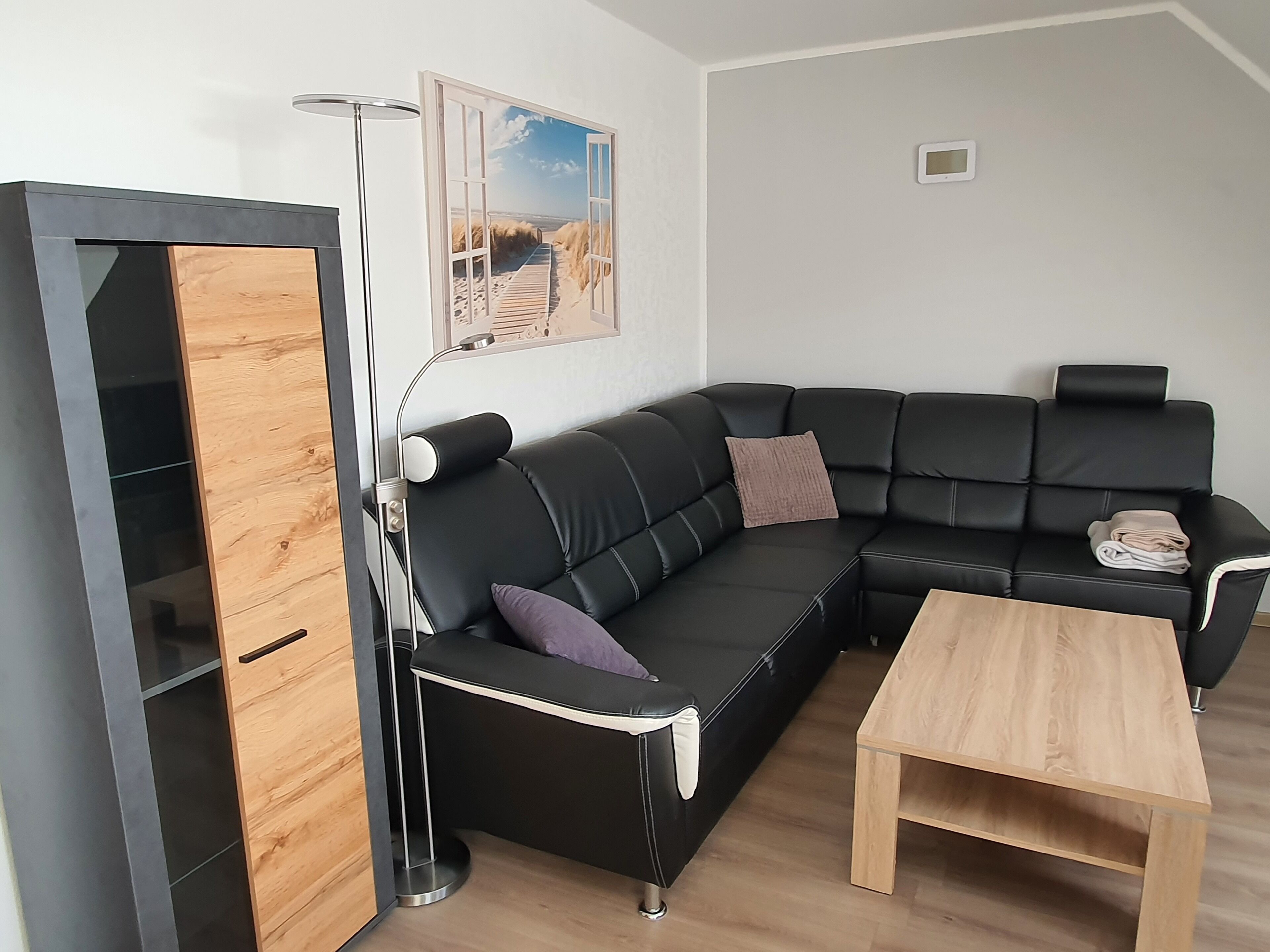 Ein modernes Wohnzimmer mit einer schwarzen Ledersofa, einem Holztisch und einer Stehlampe.
