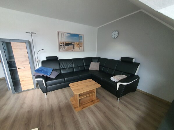 A modern living room with a black leather sectional sofa, a wooden coffee table, and a painting of a beach scene.