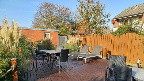 Une terrasse en bois avec une table et des chaises, entourée d’une clôture en bois et de plantes.
