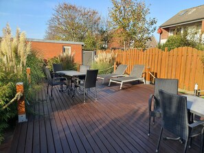 A wooden deck with a table and chairs, surrounded by a wooden fence and vegetation.