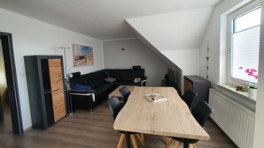 Un espace de vie moderne avec une table à manger en bois, un canapé en cuir noir et un fauteuil noir qui apporte une touche d’originalité. Une petite table sur laquelle est posé un objet décoratif se trouve dans un coin.