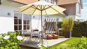 A patio with a table and chairs, a striped lounge chair, and a large umbrella. - Sealounge Vacation Home Near the Beach, Sauna, Beach Chair, Free Wi-Fi - SEASIDE - (Rosenhagen)