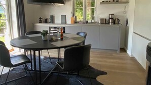 A modern kitchen with a dining area, featuring a round table, chairs, and a large black pendant light. - Sealounge Vacation Home Near the Beach, Sauna, Beach Chair, Free Wi-Fi - SEASIDE - (Rosenhagen)
