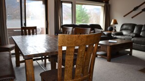 A wooden dining table with chairs, a leather sofa, and a coffee table in a room with large windows and a view of the outdoors. - Wilderness Mountain Resort, Amazing Views In White Mountains On Kancamagus Hwy (Lincoln)