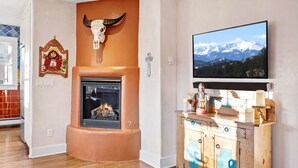 A cozy living room with a fireplace, a mounted TV, and a wooden cabinet with a cross design. - Pristine, art-filled Home 2 blocks to Historic Santa Fe Plaza. Read the reviews! (Santa Fe)