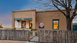 A two-story building with a beige facade, a wooden fence, and a tree with bare branches. - Pristine, art-filled Home 2 blocks to Historic Santa Fe Plaza. Read the reviews! (Santa Fe)