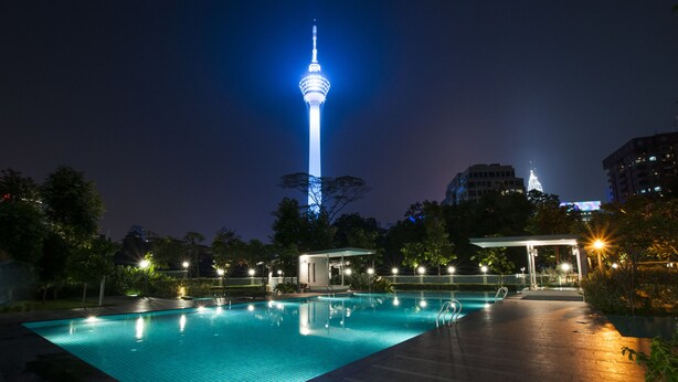 A nighttime swimming pool with a tower in the background. - AirPorter Bukit Bintang Residence (Kuala Lumpur)