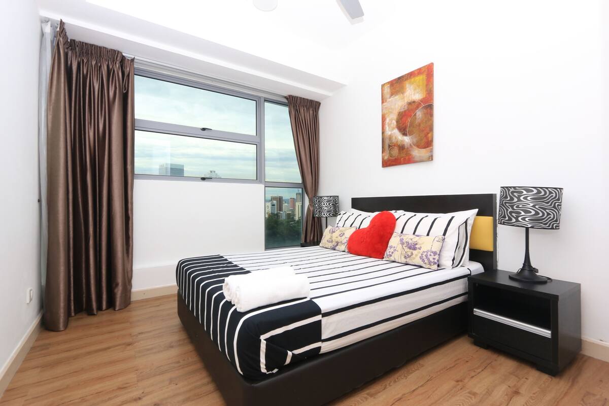 Habitación de hotel moderna con una cama grande, una mesita de noche, una ventana con cortinas y vistas a la ciudad.