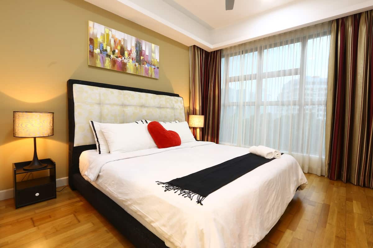 Habitación de hotel con una cama grande, dos lámparas de noche, un cuadro de un paisaje urbano y vistas a través de cortinas translúcidas.