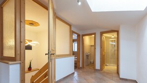 A spacious hallway with a wooden staircase, a skylight, and a bathroom visible in the background. - Rental Ban Brösign - holiday idyll with style and modern comfort (Umhausen)