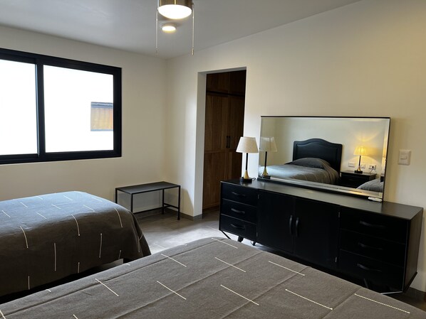 A hotel room with two beds, a dresser, a mirror, and a small table.