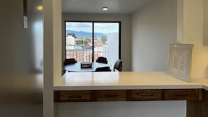 A modern kitchen with a large window, a dining table, and a framed menu on the wall.