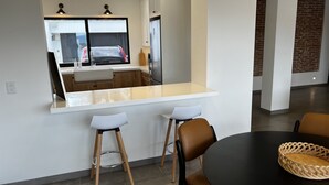 A modern kitchen with a large window, a white countertop, and two stools.
