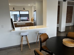 A modern kitchen with a large window, a white countertop, and two stools.