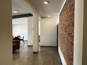 A modern interior with a brick accent wall, a dining area with a brown leather couch, and a kitchen in the background.