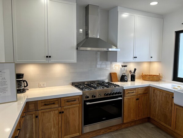 A modern kitchen with white cabinets, a stainless steel range hood, a gas stove, and an oven.