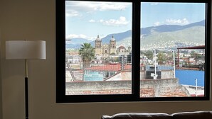 A room with a large window offering a view of a cityscape, including a church and mountains.