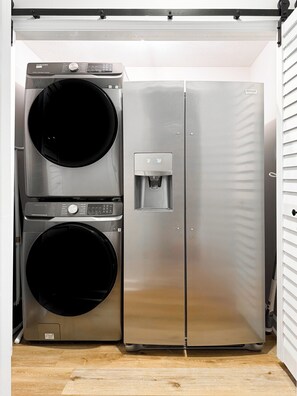 Una lavanderia compatta in acciaio inox, con lavatrice e asciugatrice integrate, un dispenser d'acqua e un piccolo armadietto.