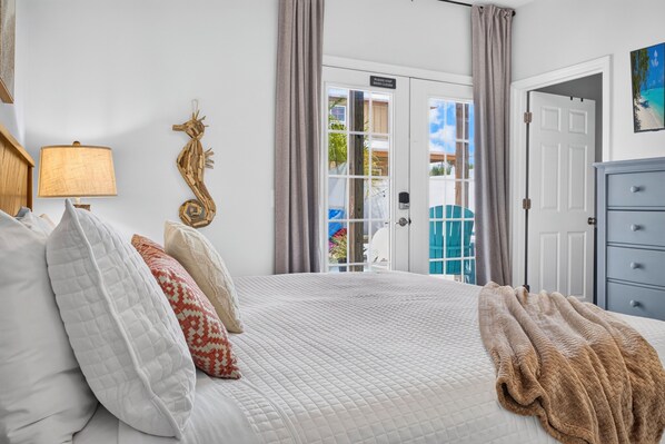 A bedroom with a bed, pillows, a lamp, a seahorse decoration, and a view through a door.