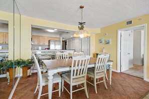 Un coin repas avec une table et des chaises en bois, un luminaire suspendu et une cuisine en arrière-plan.