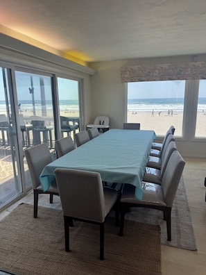 Una habitación con una mesa grande, sillas, vista a la playa y una ventana decorada con una mariposa.