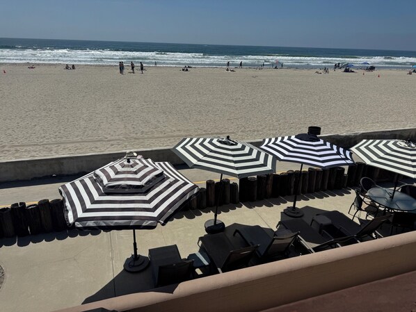 Un patio frente a la playa con sombrillas a rayas y sillones reclinables, con vista al océano.