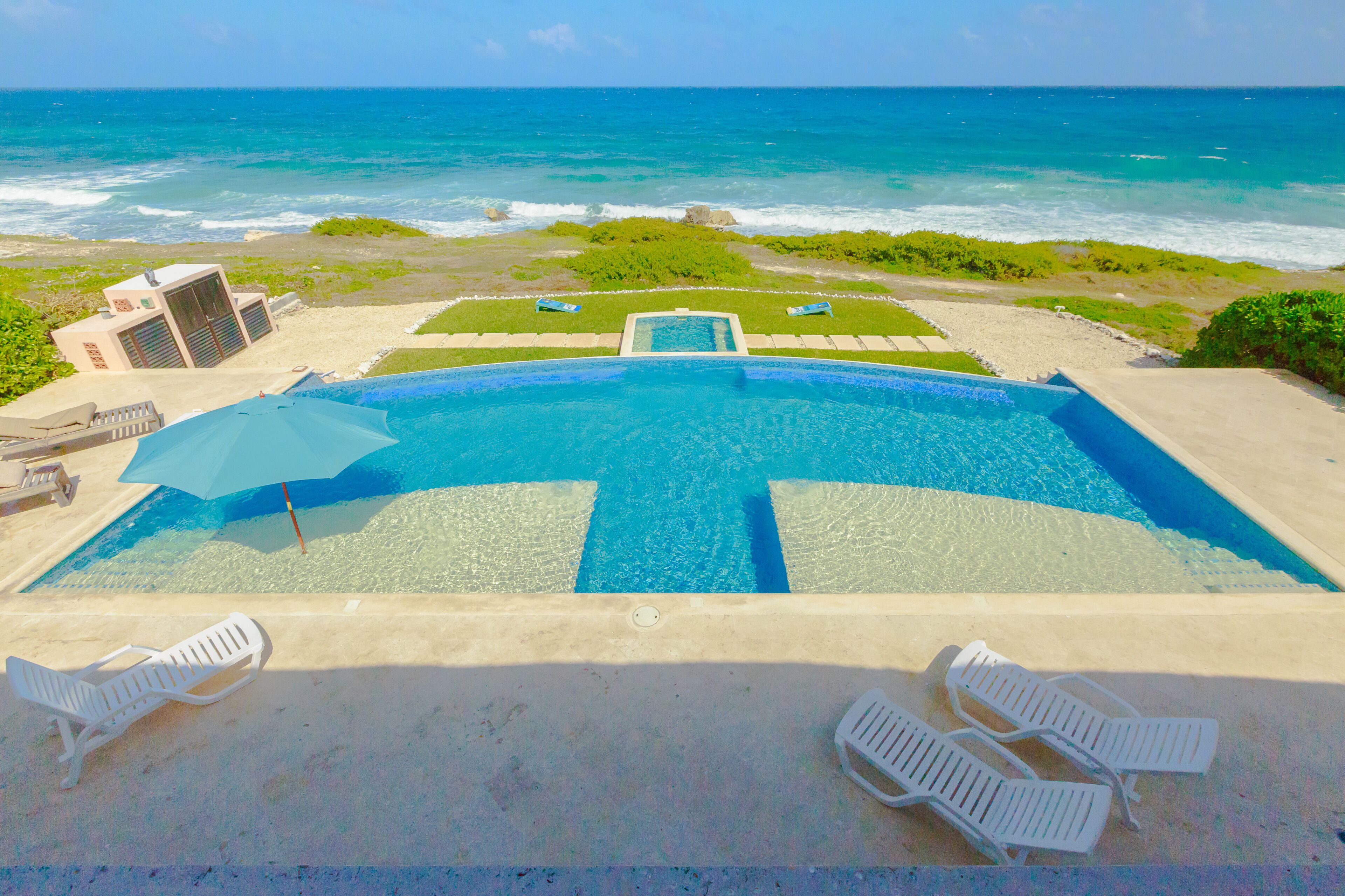 A swimming pool with a view of the ocean, surrounded by lounge chairs and a small building.