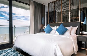 Habitación de hotel moderna con una cama grande, una mesita de noche, un escritorio y vistas al océano.