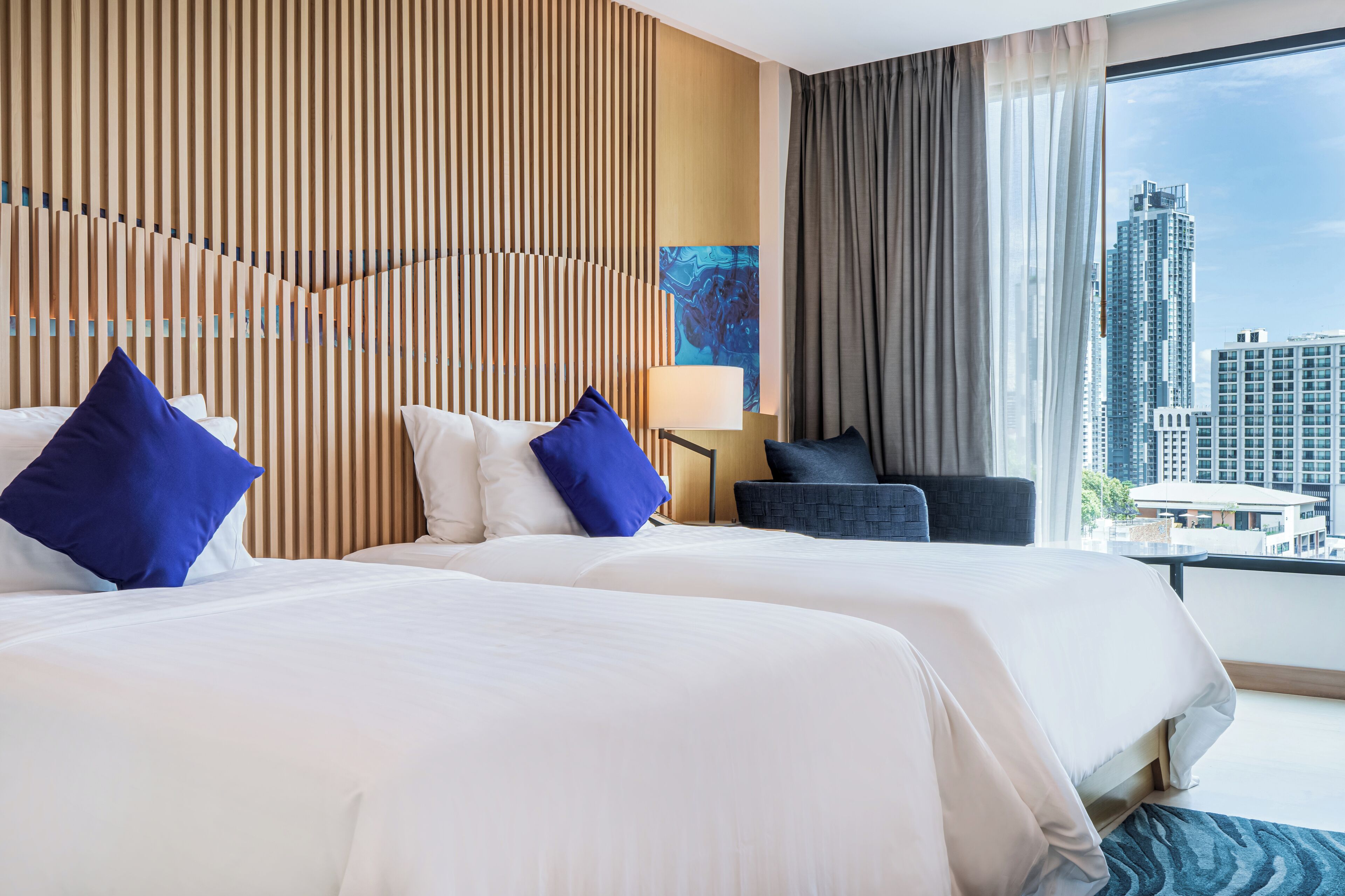 A hotel room with two beds, a city view, a modern wall design, and a lamp.