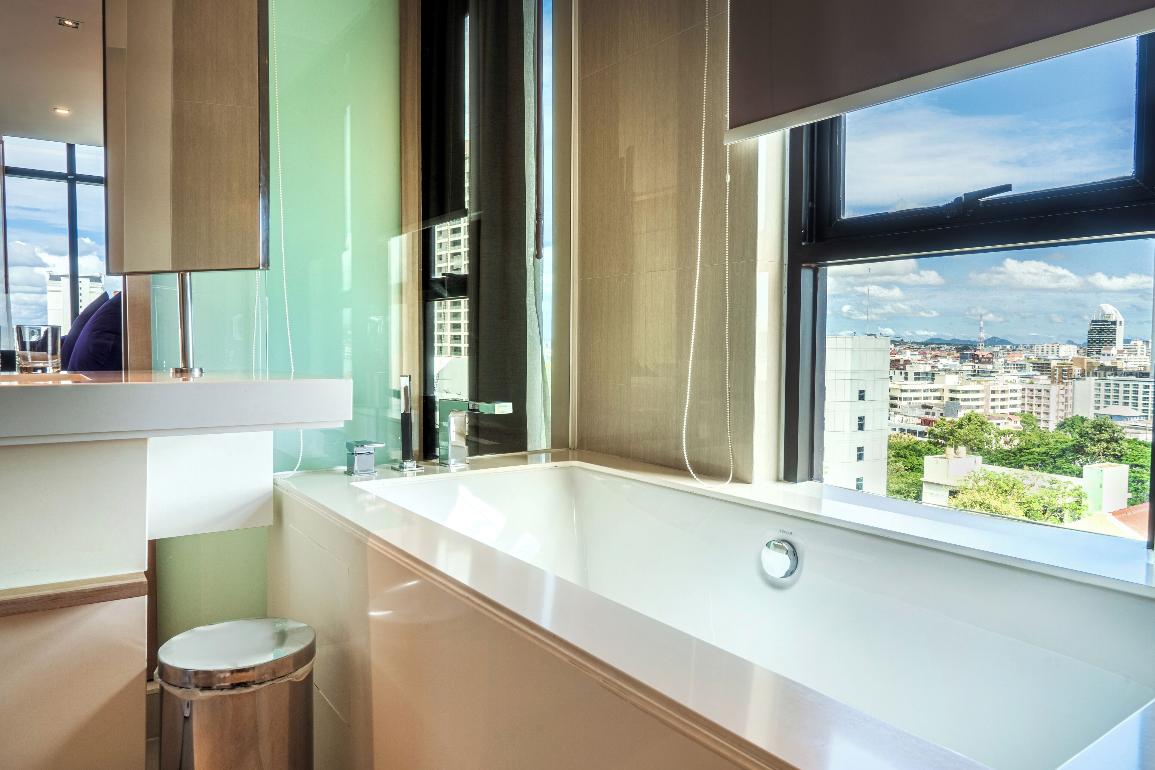 Ein modernes Badezimmer mit einer großen Badewanne, einem Fenster mit Blick auf die Stadt und einem Spiegel über dem Waschbecken.