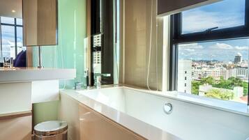 Ein modernes Badezimmer mit einer großen Badewanne, einem Fenster mit Blick auf die Stadt und einem Spiegel über dem Waschbecken.